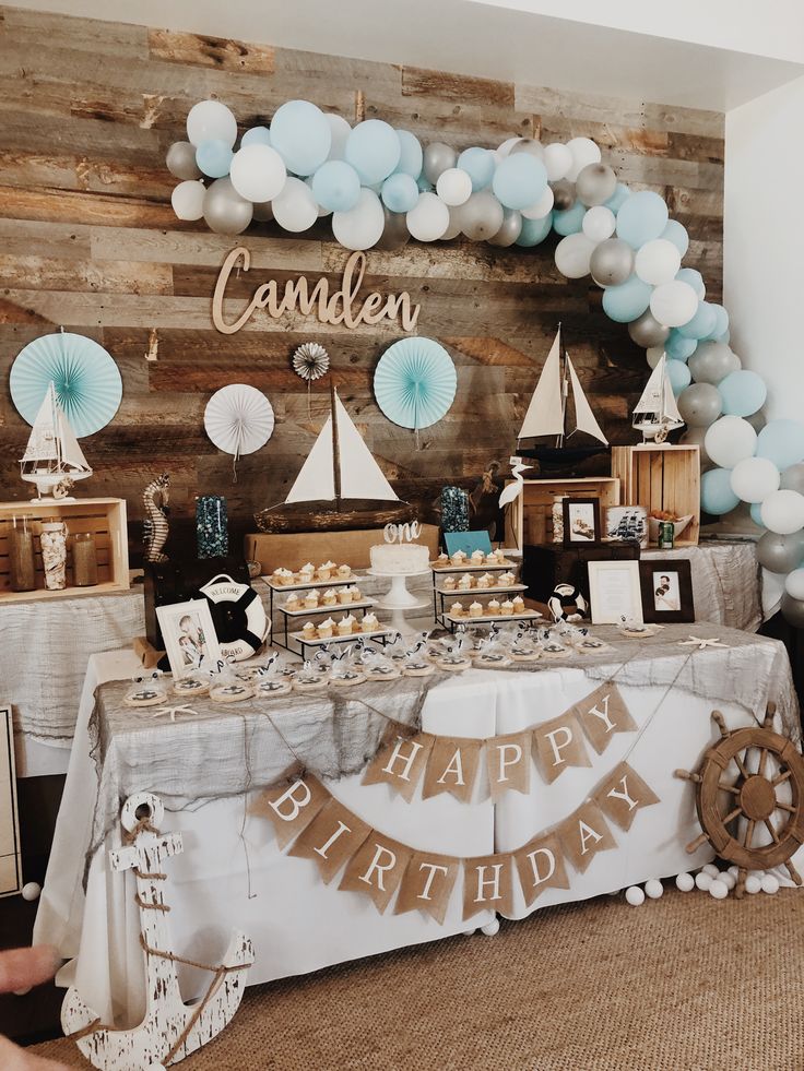 a table topped with lots of cake next to a wall covered in balloons and decorations