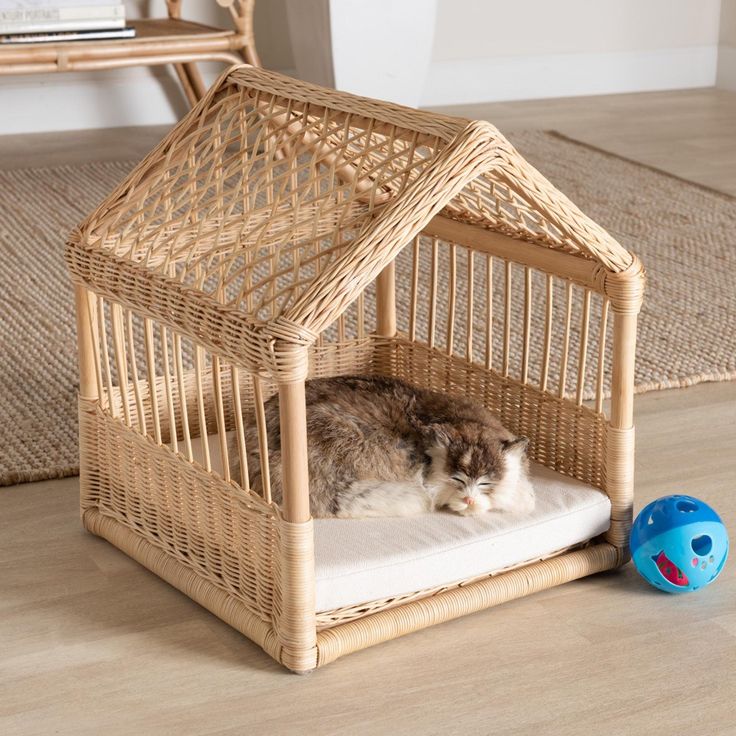 a cat laying in a wicker dog house on the floor next to a blue ball