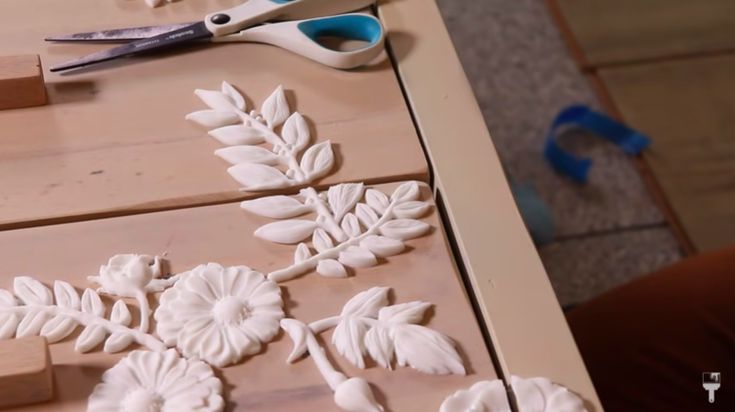 a pair of scissors and some white flowers on top of a piece of plywood