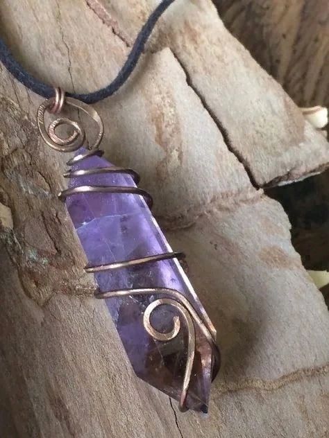 a wire wrapped pendant with a purple stone on it sitting on a piece of wood