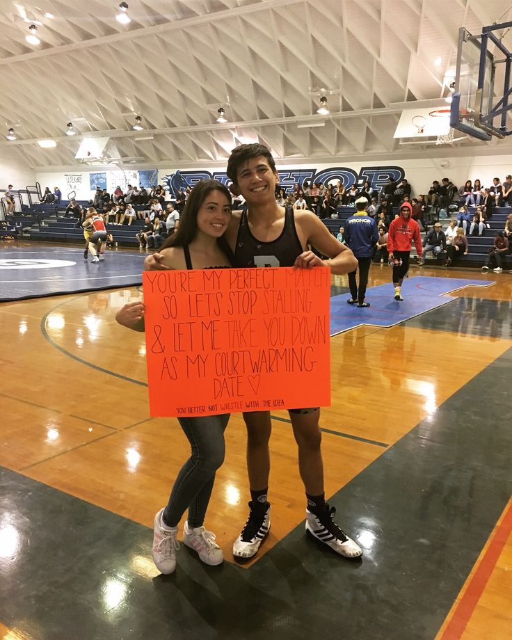 two people standing on a basketball court holding a sign