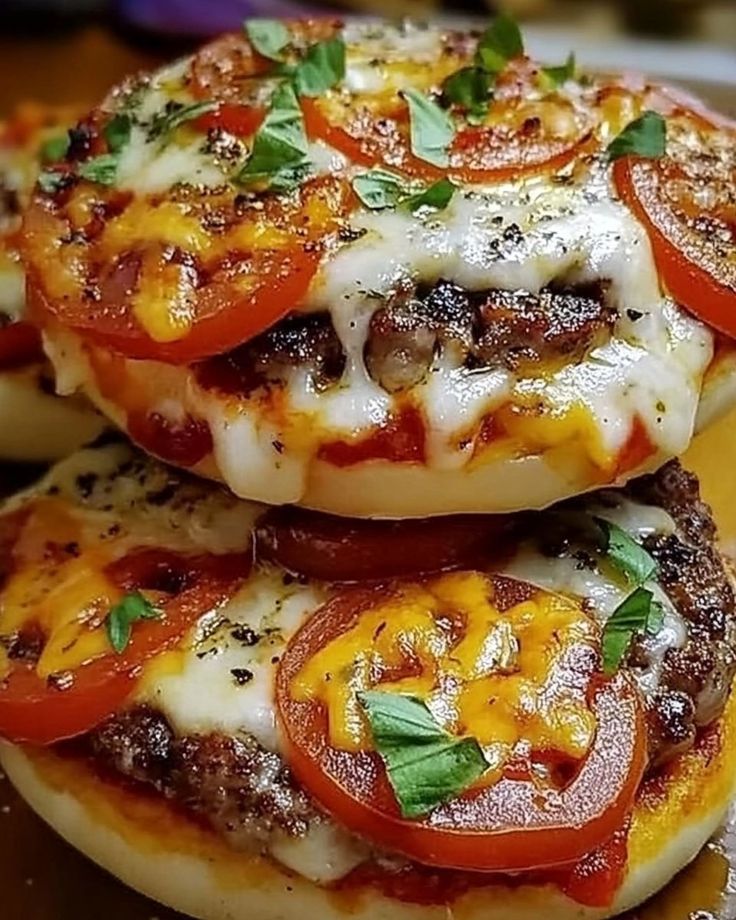 three cheeseburger burgers stacked on top of each other with tomatoes and basil