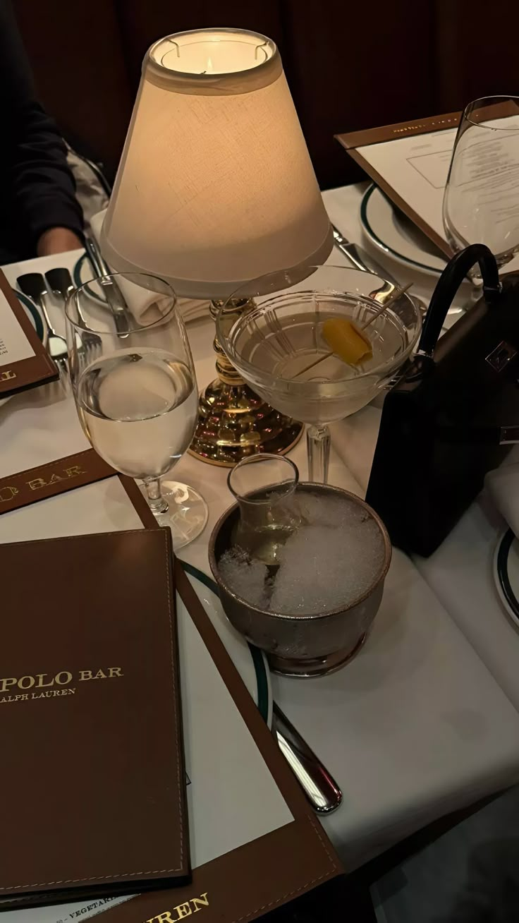 a table topped with wine glasses next to a lamp and menus on top of it