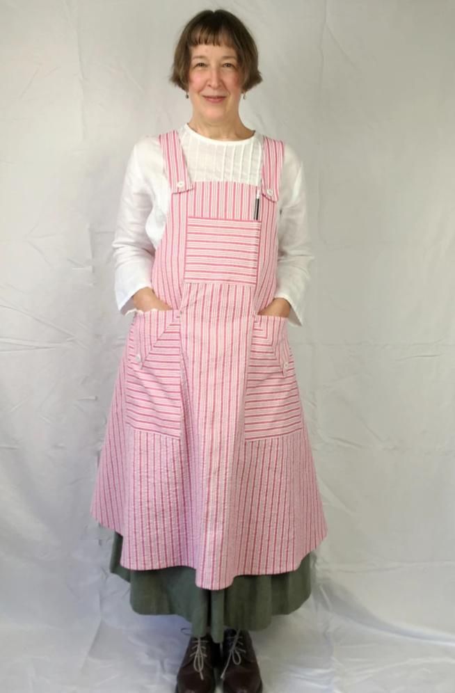 a woman standing in front of a white backdrop wearing a pink and green striped apron