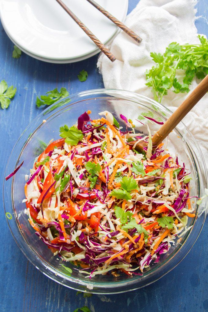 a glass bowl filled with coleslaw slaw next to a wooden spoon on top of a blue table