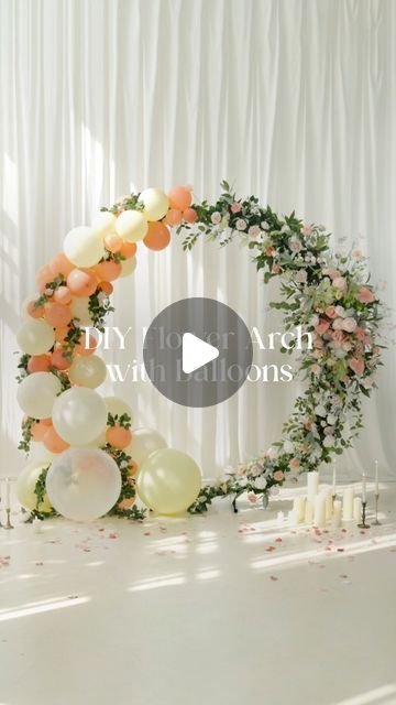 a white table topped with lots of balloons next to a wreath filled with flowers and candles