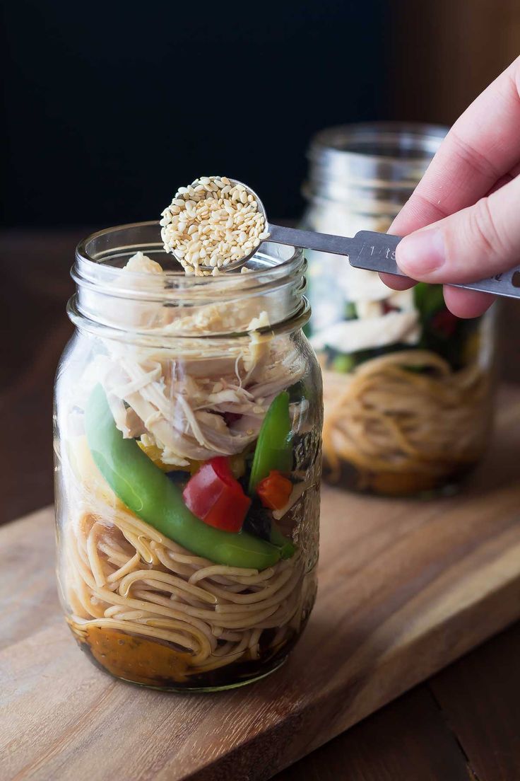 a person is spooning food into a jar filled with noodles and veggies