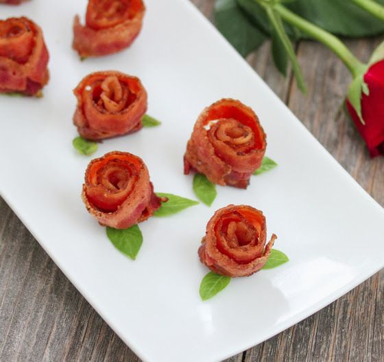 small appetizers with bacon and green leaves on a white plate next to red roses