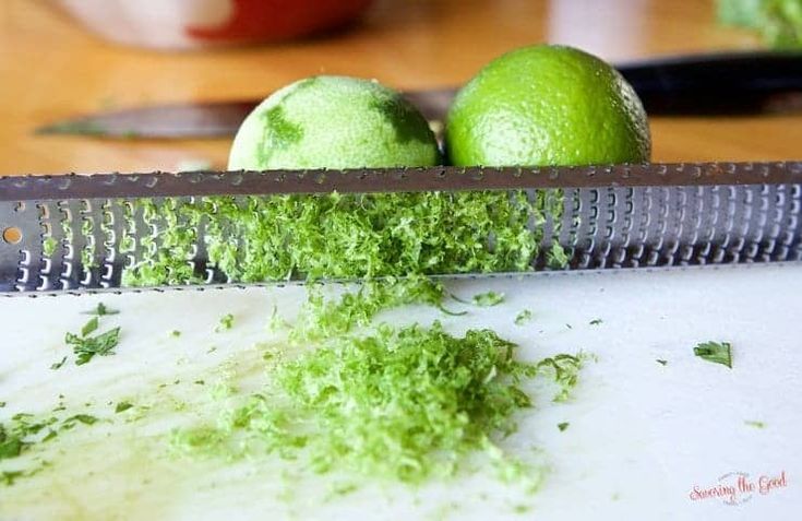 two limes sitting on top of a cutting board next to a knife and some green stuff