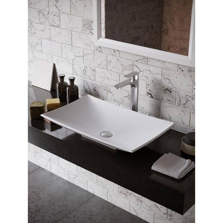 a bathroom sink sitting on top of a black counter next to a mirror and soap dispenser