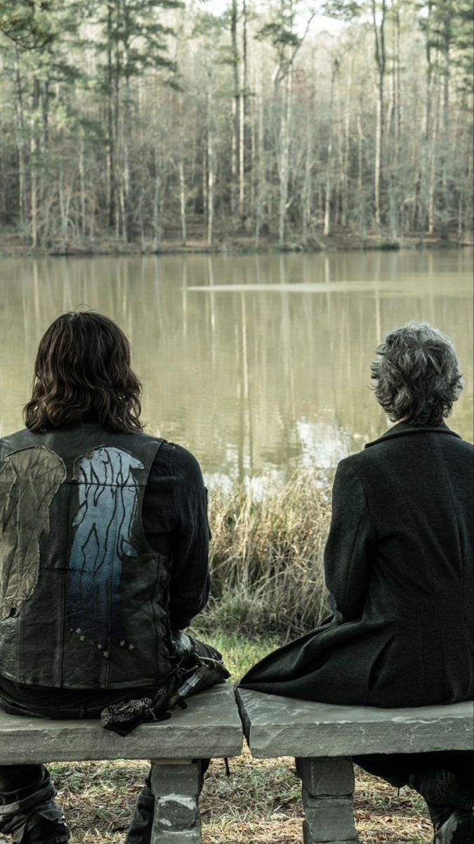 two people are sitting on a bench looking at the water