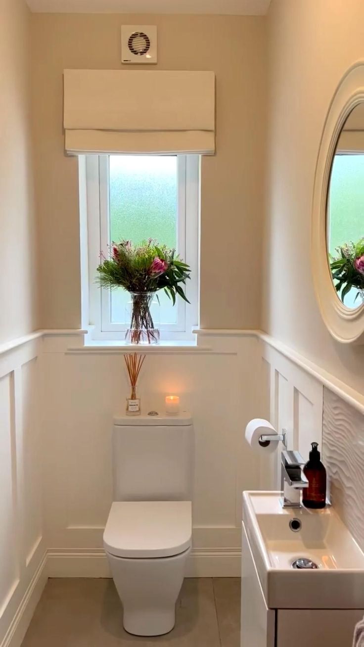 a white toilet sitting in a bathroom next to a sink under a window with flowers on it