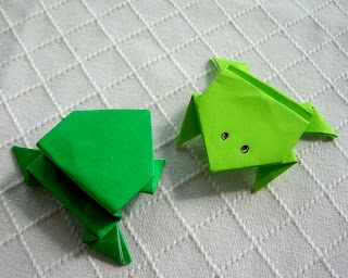 two green origami fish sitting next to each other on a white surface,