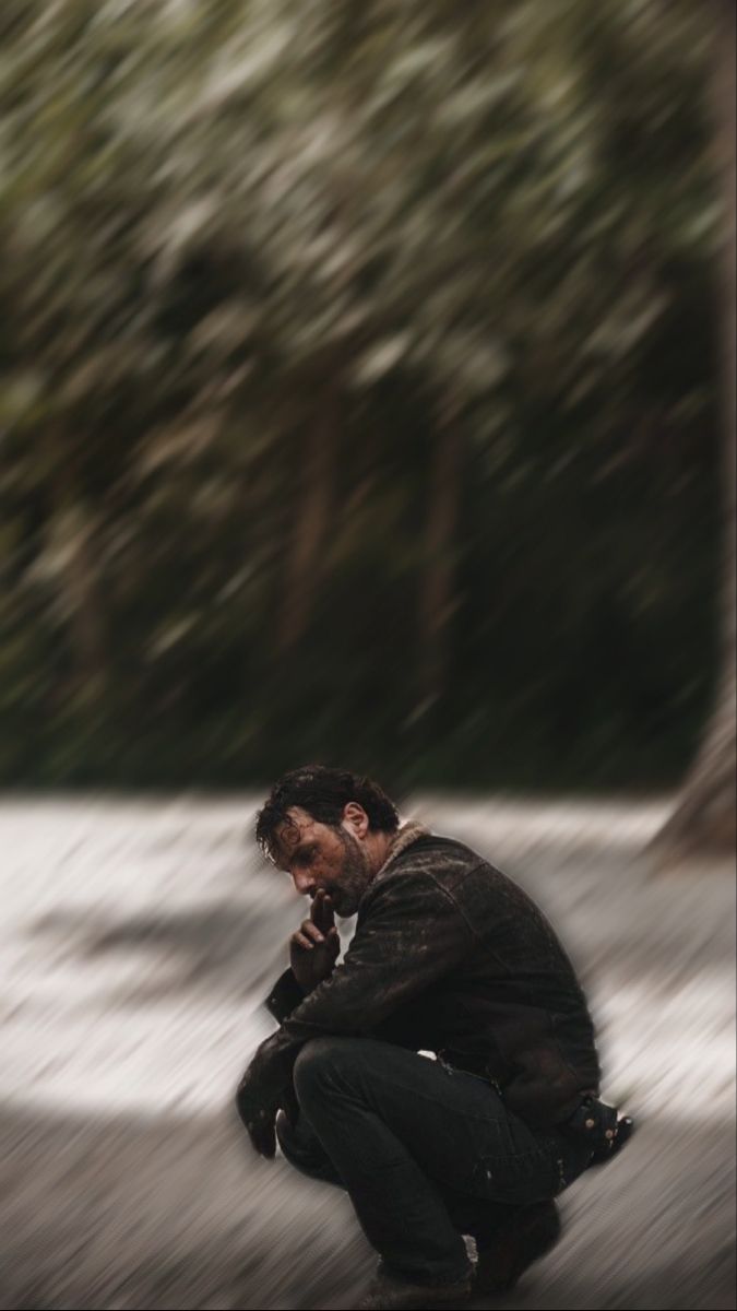 a man squatting down in the snow with his hand on his face while looking at something