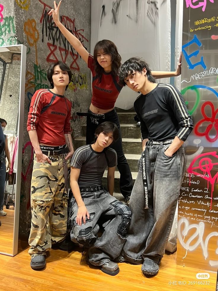 four people standing in front of a mirror with graffiti on the wall behind them and one person pointing