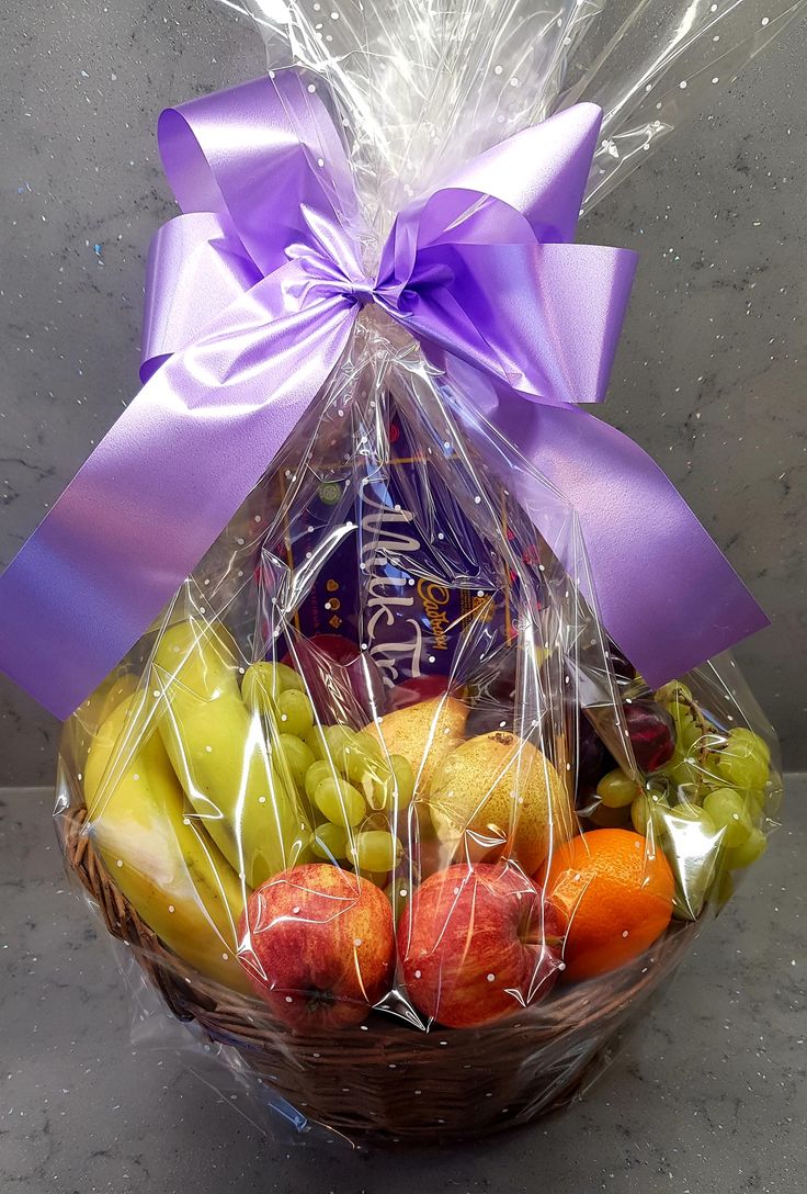 a basket filled with assorted fruit wrapped in cellophane and tied with a purple ribbon