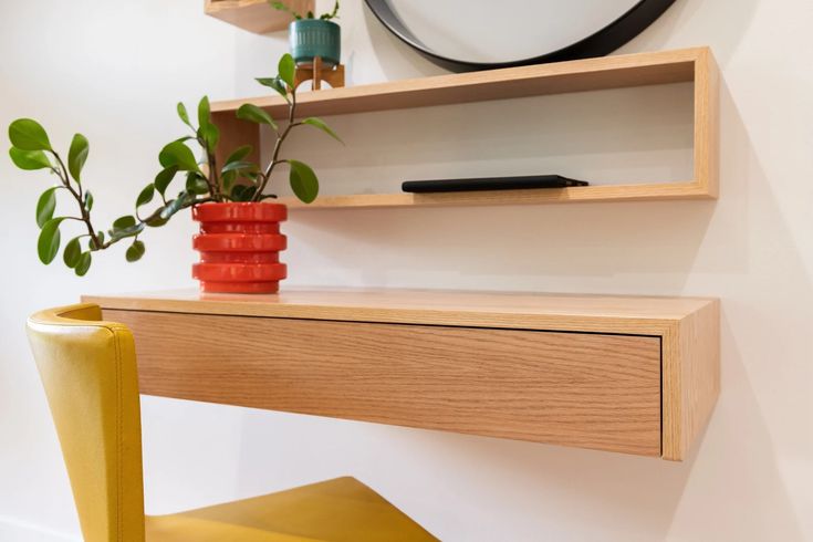 a wooden desk with a yellow chair and plant on it in front of a white wall