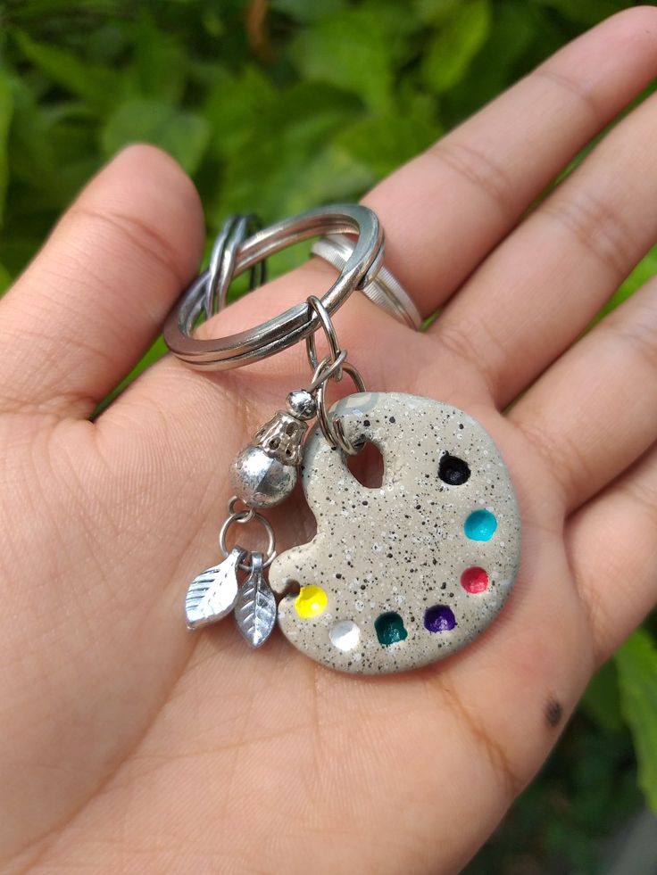 a hand holding a keychain with a painted rock on it's side