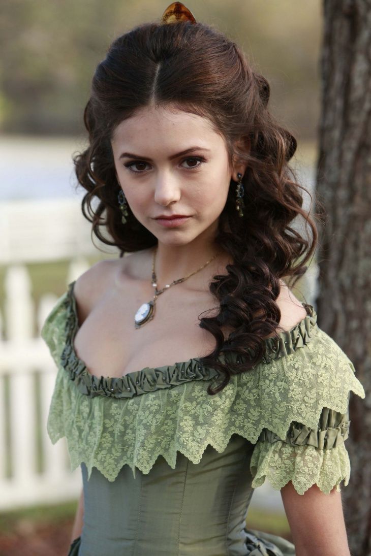 a woman in a green dress standing next to a tree