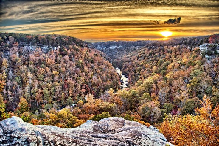 the sun is setting over a valley with trees and rocks in front of it,