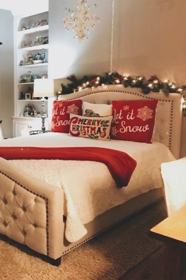 a bedroom decorated for christmas with red and white pillows on the bed, lights around the headboard