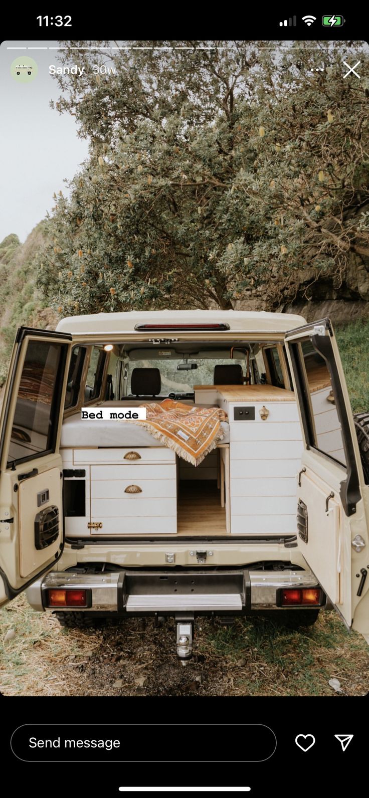 the back end of an old white van parked in a field with trees and grass