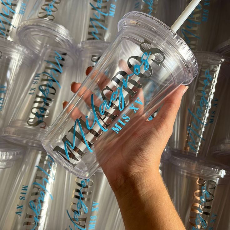 a hand holding a clear cup with blue lettering on it and straws in the background