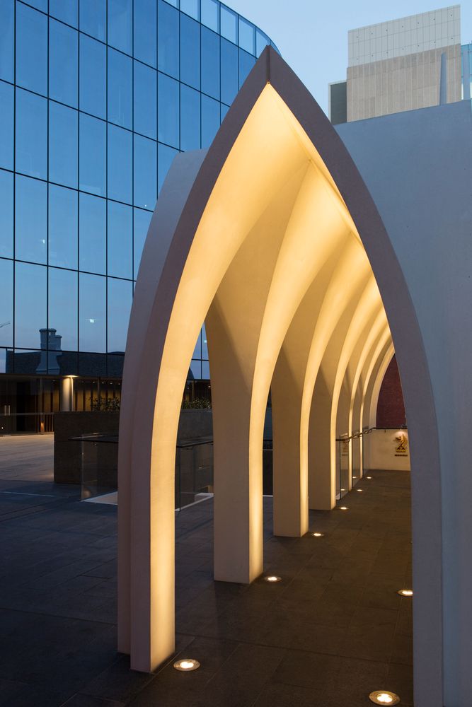 an arch with lights on it in front of a tall building at night, next to a walkway