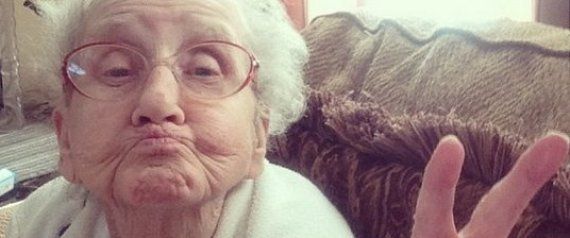 an older woman sitting on a couch making the peace sign