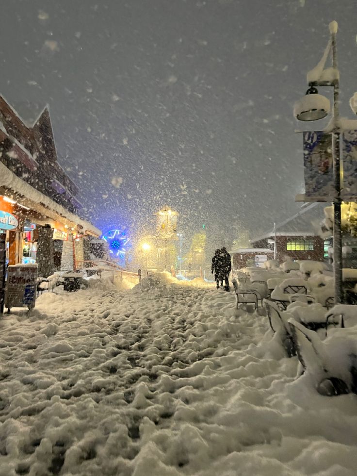 people walking down a snow covered street in the night time with lots of snow on the ground