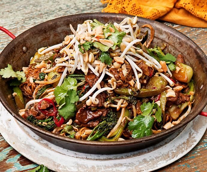 a bowl filled with stir fry and vegetables on top of a wooden table next to a fork