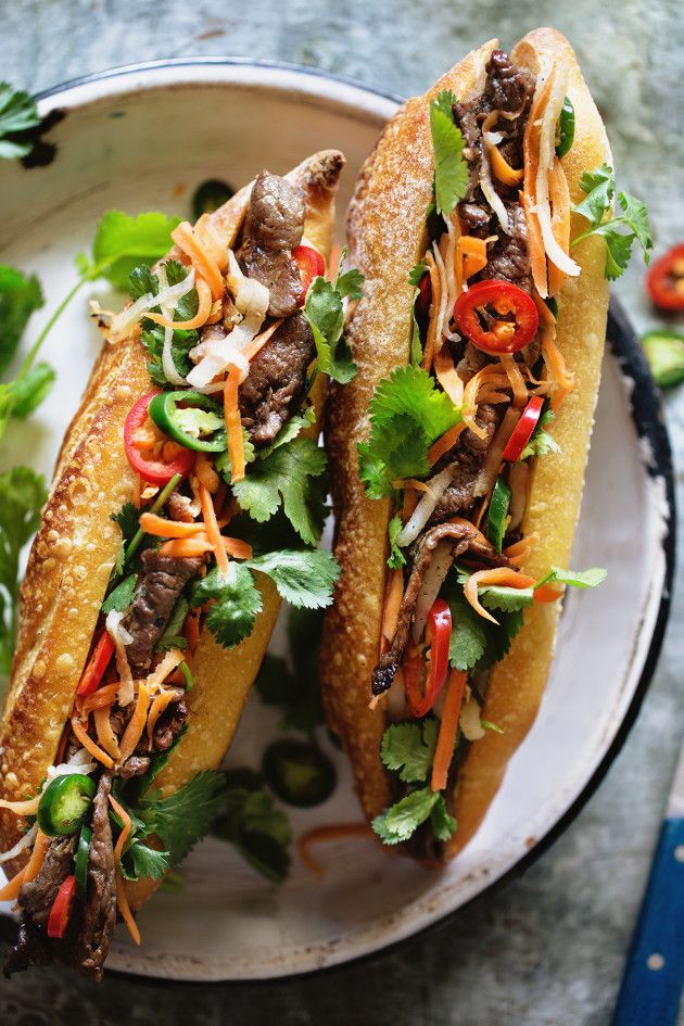 two sub sandwiches with meat and vegetables on a white plate next to some chopsticks