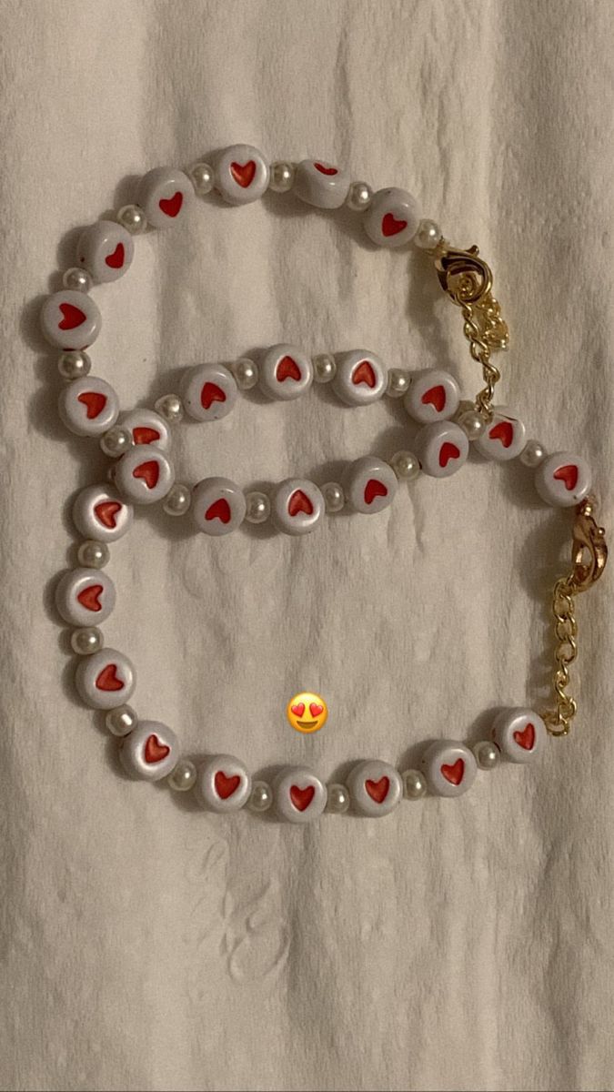 a white beaded bracelet with red hearts and a gold heart charm on the clasp