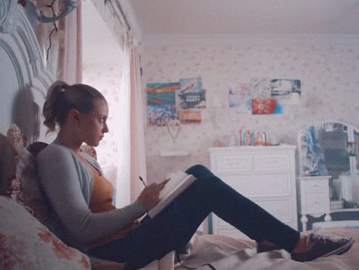 a woman sitting on top of a bed holding a pen and writing in a notebook