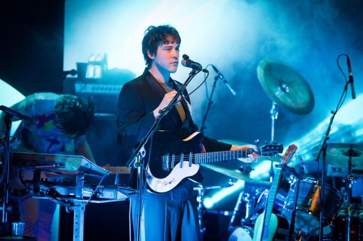 a man standing in front of a microphone while holding a guitar