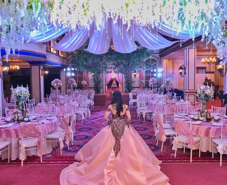 a woman in a wedding dress standing next to tables with white and pink linens