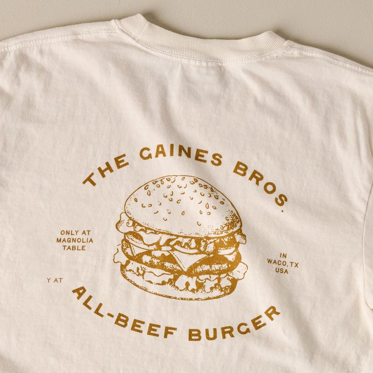 Show off your support for one of the best burgers in town with this classic ivory tee! Inspired by the fan-favorite Gaines Brothers Burger at Magnolia Table, this white tee features a playful, contrasting burger graphic that reads THE GAINES BROS ALL-BEEF BURGER. Retro Tee Design, Restaurant Tshirt Designs, Graphic Tee Inspo Design, Coffee Shop Tshirt, Burger Graphic, The Best Burgers, Best Burgers, Magnolia Table, Beef Burger