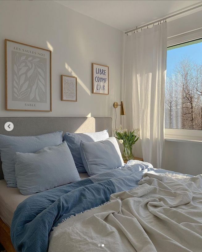 a bed with blue sheets and pillows in a bedroom next to a window that looks out onto the trees