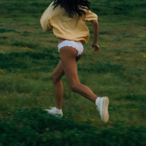 a woman in white shorts and yellow shirt playing with a frisbee on the grass