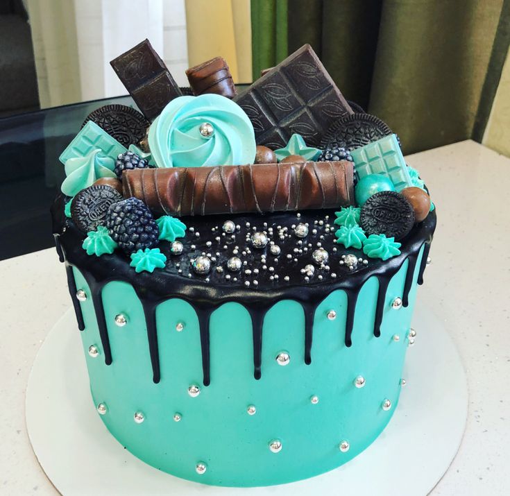 a blue and black cake with chocolate decorations on it's top, sitting on a table