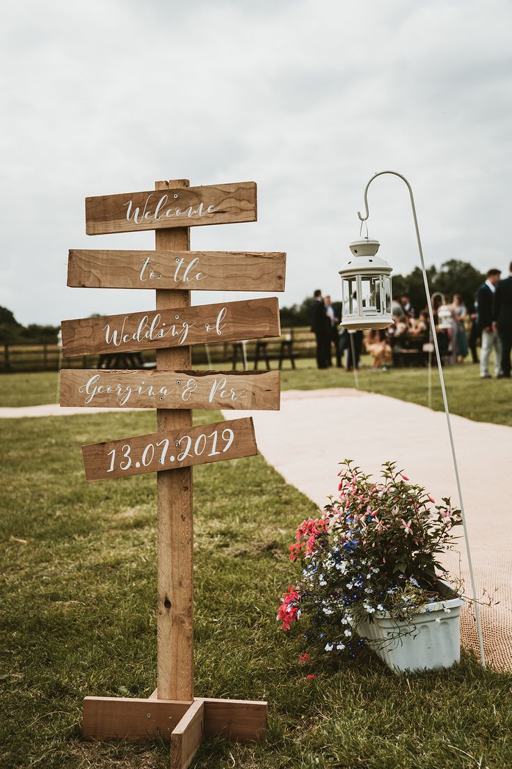 a wooden sign sitting on top of a grass covered field next to a flower pot