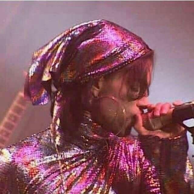 a person with a microphone in their hand and wearing a colorful outfit on top of his head