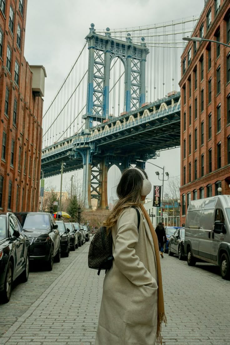 a woman is walking down the street in front of some tall buildings and a bridge