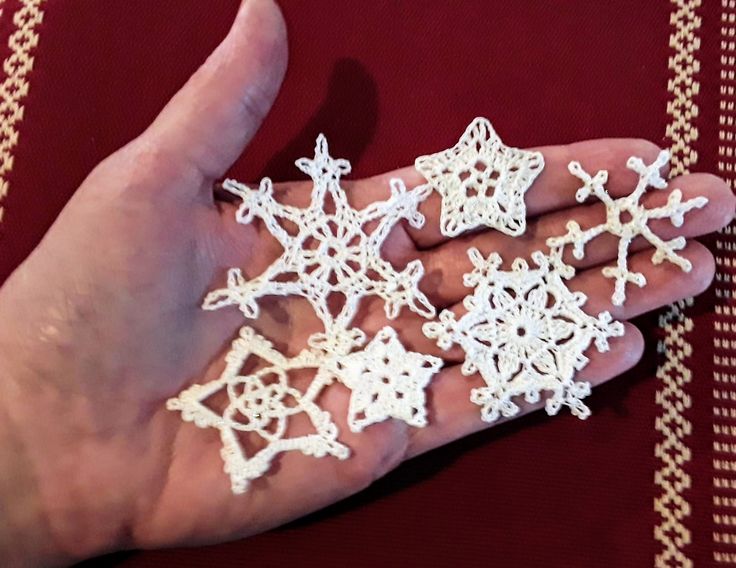 a hand is holding several snowflakes in white crochet