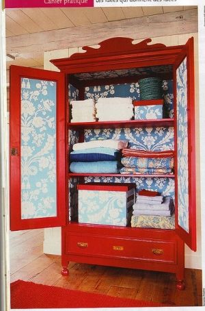 an open red cabinet with folded towels on top and blue wallpaper in the background