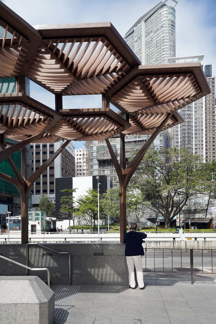 a person standing under a wooden structure in the middle of a city street with tall buildings behind them