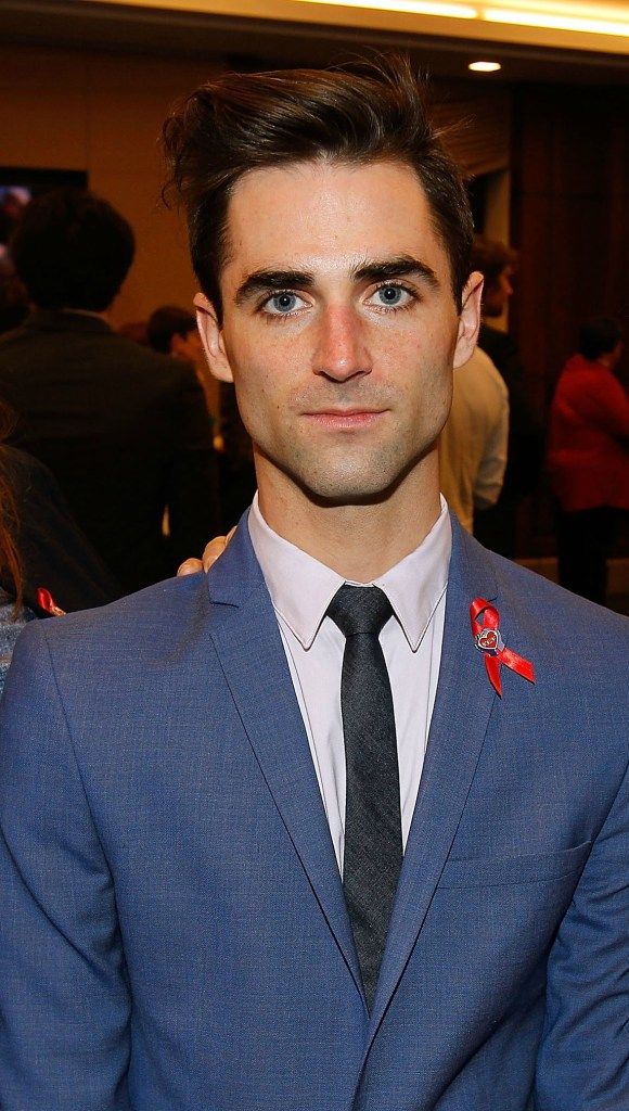 a man in a suit and tie posing for the camera with other people behind him