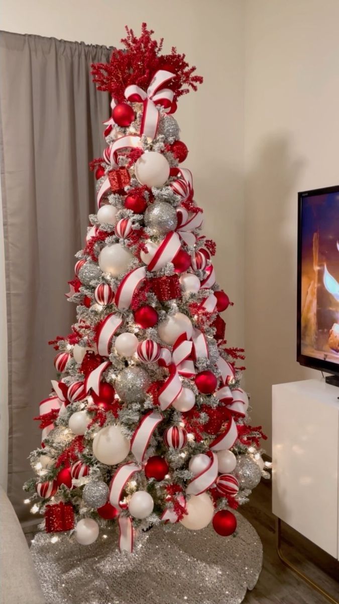 a christmas tree decorated with red and white ornaments in front of a flat screen tv