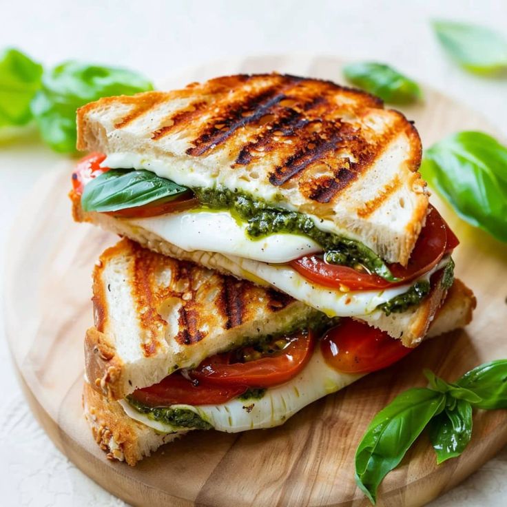 two grilled sandwiches with tomatoes, mozzarella and basil on a wooden plate