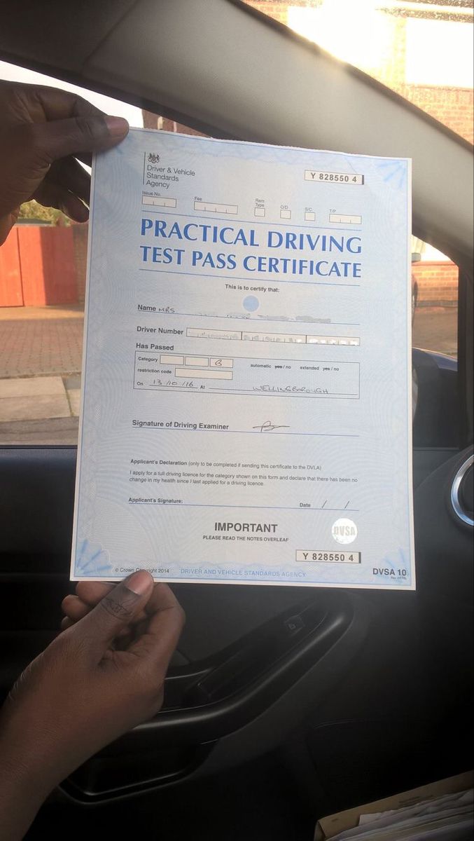 a person holding up a driving test pass in their car with the driver's hand